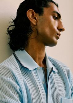 a man with long black hair wearing a blue shirt and silver earring on his neck