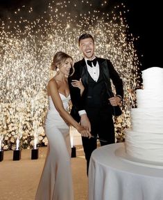 a man and woman standing next to a white cake with sparklers in the background