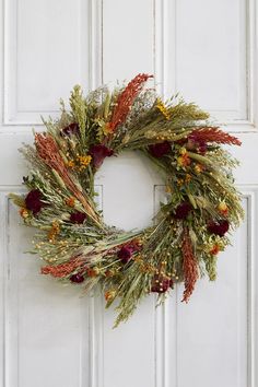 a wreath is hanging on the door with dried flowers and foliage around it, as well as other decorations