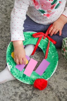 a toddler sitting on the floor with a paper plate wreath and letter cut out