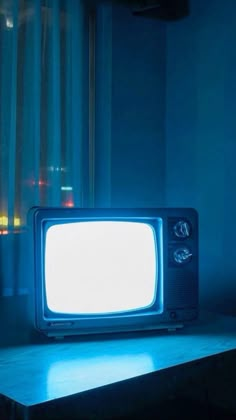 an old tv sitting on top of a wooden table in front of a window with curtains