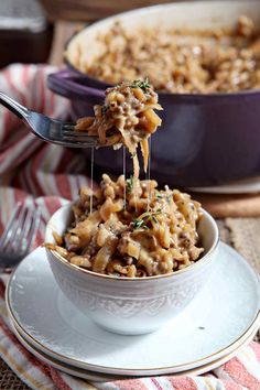 a spoon full of macaroni and cheese being lifted from a bowl with a fork