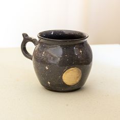 a black and gold mug sitting on top of a white counter next to a wall