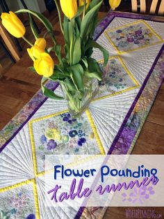 a vase filled with yellow flowers sitting on top of a table covered in quilts