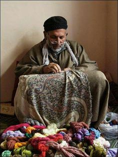 an old man sitting on the floor next to a pile of yarn