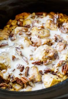 a crock pot filled with cinnamon rolls covered in icing and pecans on top