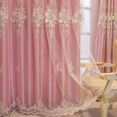 a pink curtain with white flowers on it and a chair in front of the window