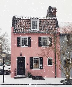 a pink house with black shutters and snow falling on the ground in front of it