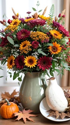 a vase filled with lots of flowers sitting on top of a table next to a white pumpkin