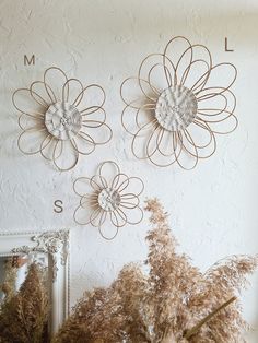 three metal flowers are mounted on the wall above a mirror and some dried grass is in front of it