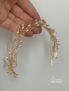 a hand holding a gold leaf and pearl hair comb