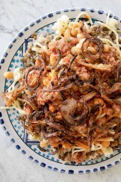 a bowl filled with pasta and meat on top of a white marble countertop next to a blue and white polka dot plate