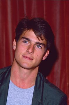 a young man is posing in front of a red curtain with his eyes wide open