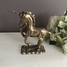 a gold unicorn figurine next to some flowers on a white table with grey walls