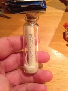 a hand holding a tiny bottle filled with sand on top of a wooden table next to candy