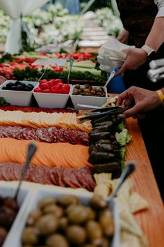 people are serving themselves food at an outdoor buffet