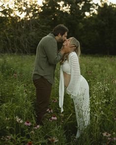 a man and woman kissing in the middle of a field with wildflowers at sunset