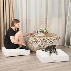 a woman sitting on the floor next to a small dog and looking at her magazine