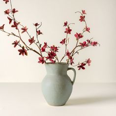 a vase filled with red flowers sitting on top of a white table next to a wall