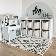 a play room with toy kitchen and storage bins on the floor next to it