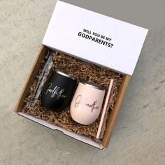 two black and pink coffee mugs in a cardboard box with writing on the side