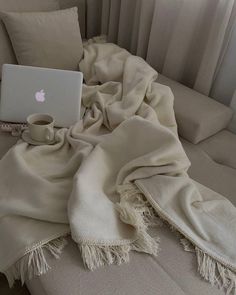 an open laptop computer sitting on top of a white couch next to a cup of coffee