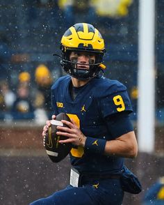 a man holding a football on top of a field in the rain with other people watching