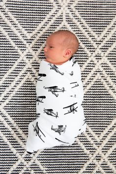 a baby wrapped in a swaddle laying on top of a rug next to a wall