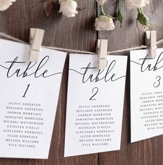 wedding seating cards hanging from clothes pins on a wooden wall with white flowers in the background