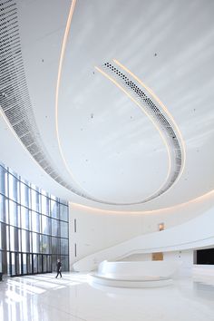 a person walking in an empty room with white walls and ceiling lights on either side