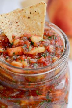 a glass jar filled with salsa and a tortilla chip sticking out of it