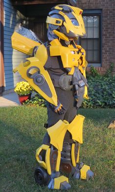 a person in a costume that looks like a yellow and gray robot standing on the grass