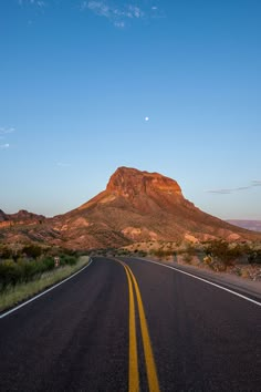 an empty road in the middle of nowhere with mountains in the background at sunset or sunrise