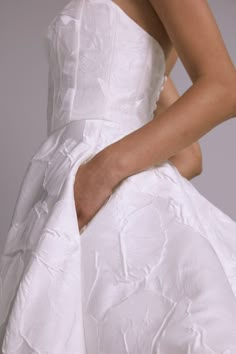 a woman in a white wedding dress with her hand on the back of her dress