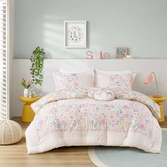 a white bed with pink and blue comforters in a room next to a potted plant