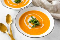 two bowls of carrot soup on a white table