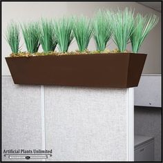 some green plants are in a brown planter on a white wall near an office cubicle