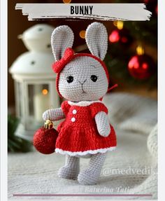 a small crocheted rabbit in a red dress holding a christmas ornament