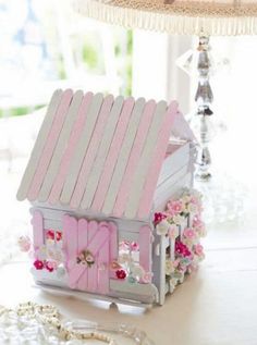 a pink and white birdhouse with flowers on the roof is sitting on a table