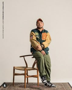 a man sitting on top of a wooden chair in front of a white wall,