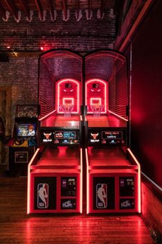 two arcade machines with neon lights on them in a room filled with wooden floors and red walls