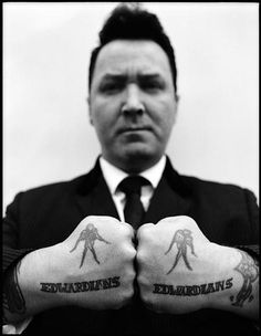 a man in a suit and tie holding two hands with tattoos on them