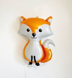 an orange and white balloon shaped like a fox with its tail hanging from the wall