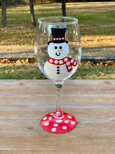 a wine glass with a snowman painted on the side sitting on a wooden table