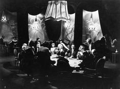 a group of people sitting around a table in front of some lights and curtains on the wall