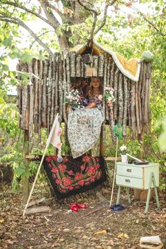 a woman is sitting in a small wooden structure with flowers on it and clothes hanging out to dry