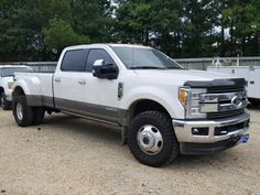 a large white truck parked in a parking lot next to other trucks and trailers with trees in the background