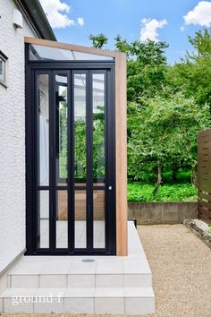 an open door on the side of a house in front of some trees and bushes