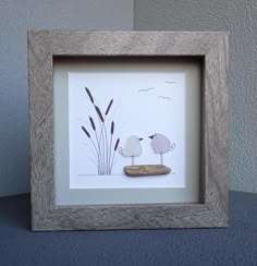 a couple of birds standing next to each other in a wooden frame on top of a table