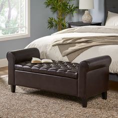 a bed with a brown leather bench sitting on top of it next to a window